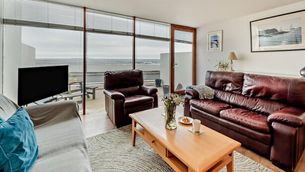 Ein modernes Wohnzimmer mit großem Fenster, einer Ledersofa, einem Couchtisch aus Holz und einem Flachbildfernseher.