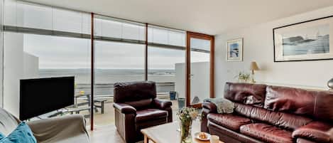 A modern living room with a large window, a leather sofa, a wooden coffee table, and a flat-screen TV.