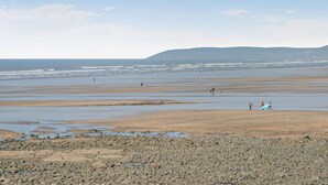 Ein Strand mit felsigem Vordergrund, einem weiten Sandgebiet und einer entfernten Bergkette.