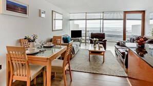 Ein modernes Wohnzimmer mit Essbereich, großen Fenstern und Meerblick.