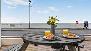 Ein Holztisch mit Frühstücksgebäck und einer Blumenvase auf einer Terrasse mit Blick aufs Meer.