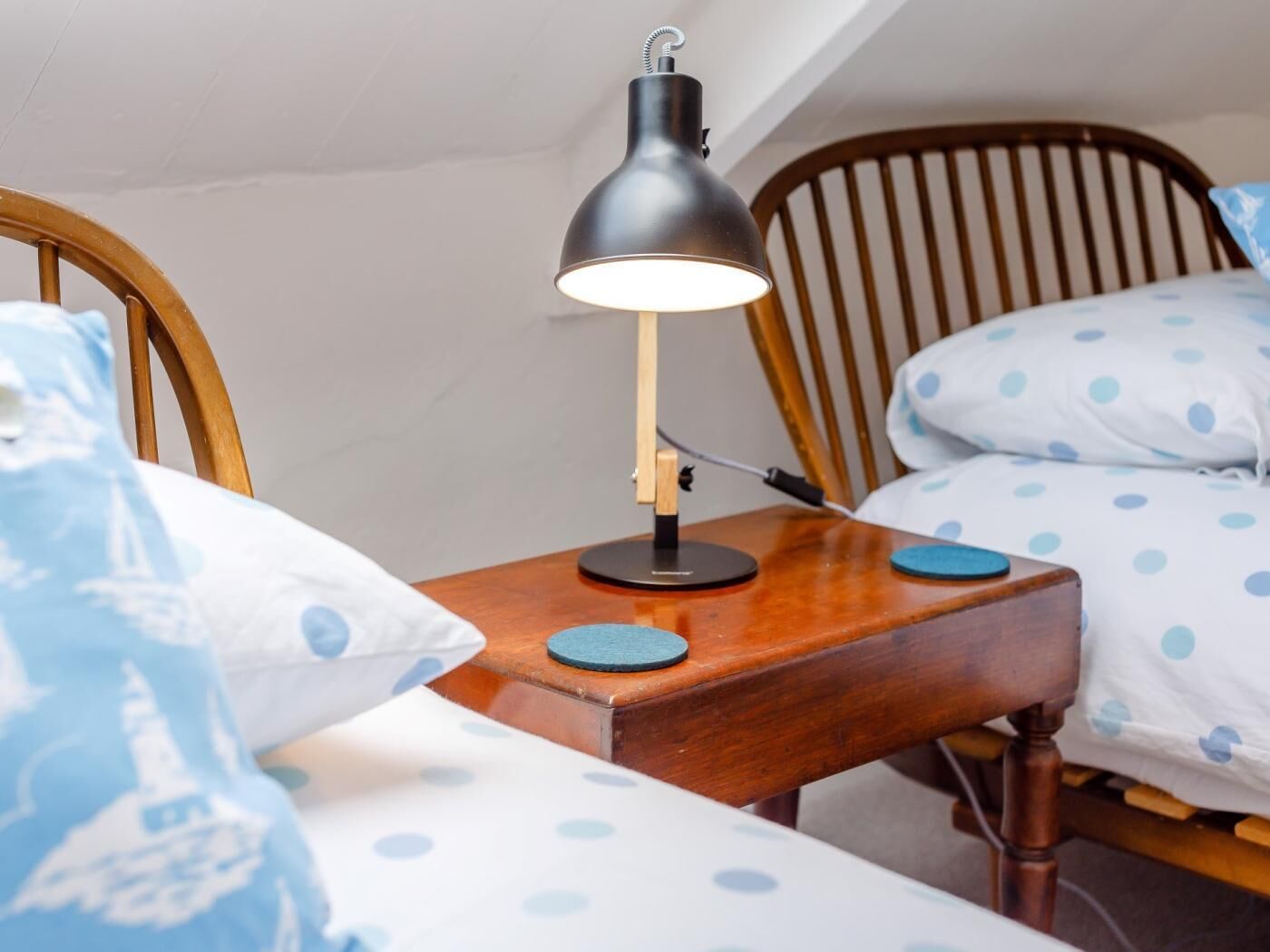 Un dormitorio con cabecera de madera, una mesita de noche con lámpara y ropa de cama con estampado de lunares.