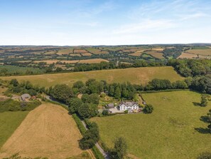 An aerial view of a rural landscape with rolling fields, a large house with a garden, and a smaller building nearby.