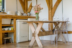 Ein rustikaler Holztisch mit Blumen in einer Vase, ein Kühlschrank und ein Stuhl in einer Küche.