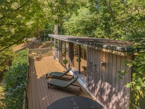 Eine Holzterrasse mit zwei Liegestühlen und einem Tisch, umgeben von dichtem Grün.