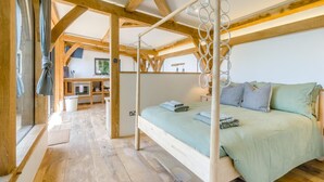 Ein Schlafzimmer mit Himmelbett, Holzbalken, einer kleinen Küchenzeile und Blick ins Freie.