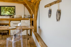 A dining area with a wooden table, chairs, and a white wall with two hanging objects. - 1 Bed in Barnstaple (oc-62134) (Swimbridge)