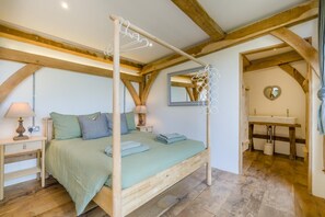 Un dormitorio con cama con dosel, una mesita de noche con lámpara, un espejo y vista a un baño con lavamanos y un espejo con forma de corazón.