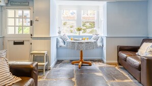 Een kamer met een stenen vloer, een vensterbank met een tafel en stoelen, een bruine leren bank en een kleine witte tafel.