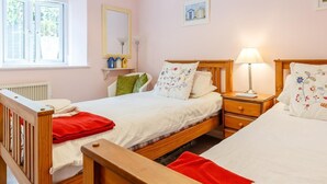 Een slaapkamer met twee bedden, een raam, een radiator, een nachtkastje met een lamp en een klein plankje met decoratieve objecten.