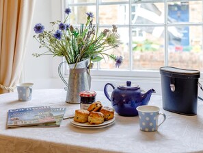 A table with a teapot, a pitcher, a plate of scones, a magazine, and a window with a view.