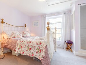 A bedroom with a bed, a radiator, a window with curtains, and a small table with a cushion. - 3 Bed in Polruan (oc-pc012) (Polruan)
