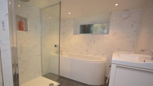 Een moderne badkamer met een glazen douchecabine, een vrijstaand bad en een wastafel met een spiegel erboven.