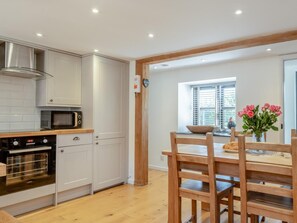 A modern kitchen with white cabinets, a built-in oven, and a microwave. There is a wooden dining table with chairs and a vase of flowers. - 2 Bed in Godshill (oc-ic149) (Godshill)