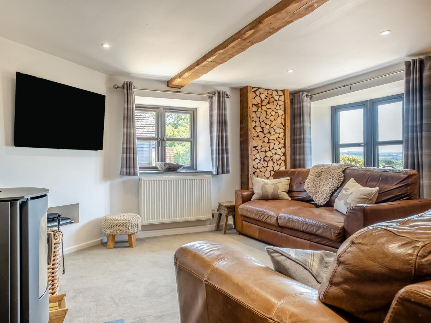 A living room with a brown leather sofa, a television mounted on the wall, and a window with curtains.