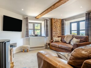 A living room with a brown leather sofa, a television mounted on the wall, and a window with curtains. - 2 Bed in Godshill (oc-ic149) (Godshill)