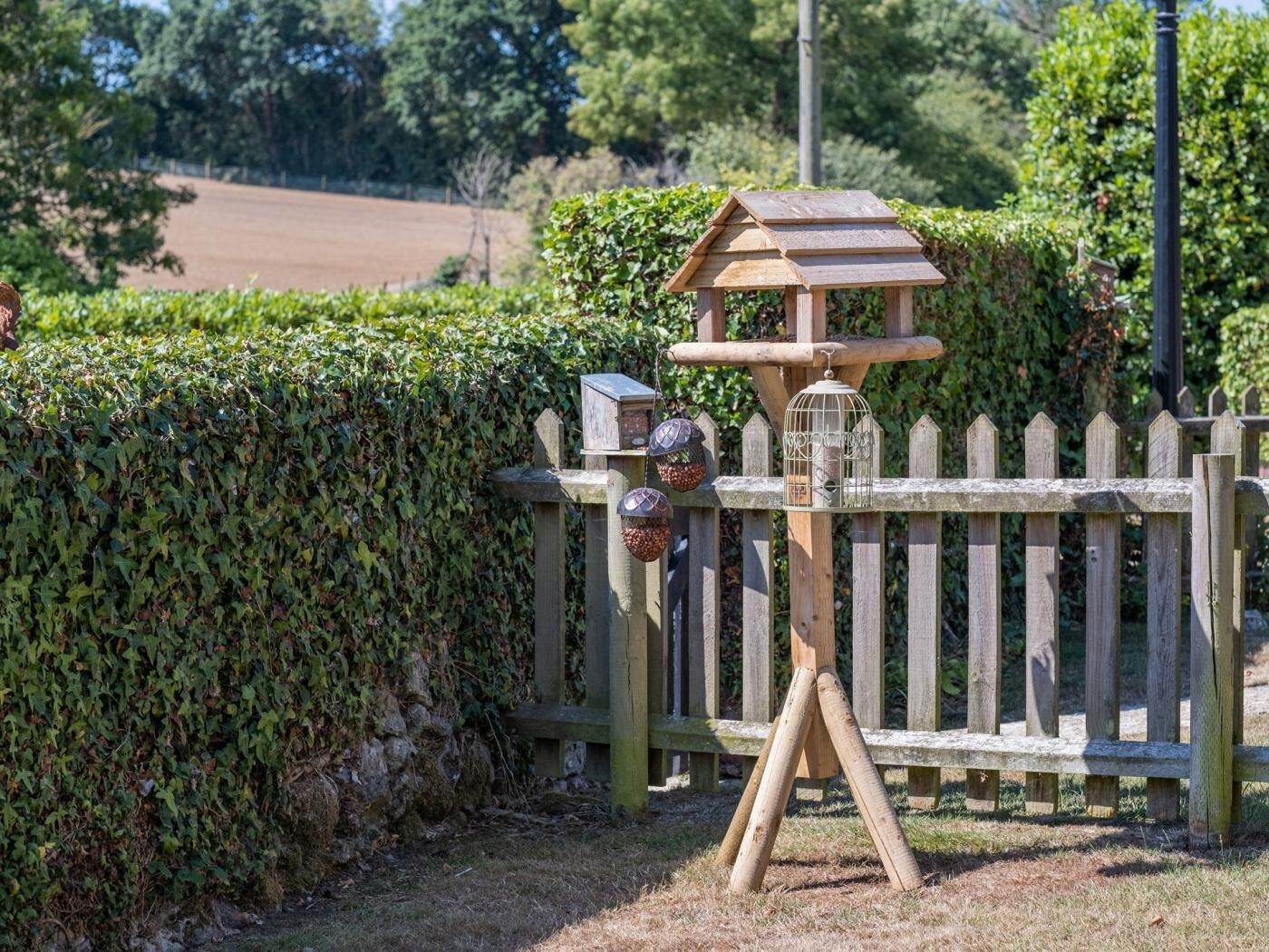 Een houten vogelhuisje met een klein huisje eraan bevestigd, een metalen voeder en een houten hek.