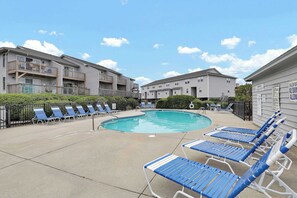 A pool area with lounge chairs, a swimming pool, and apartment buildings in the background. - Lazy Day Lookout - New Listing (Surf City)