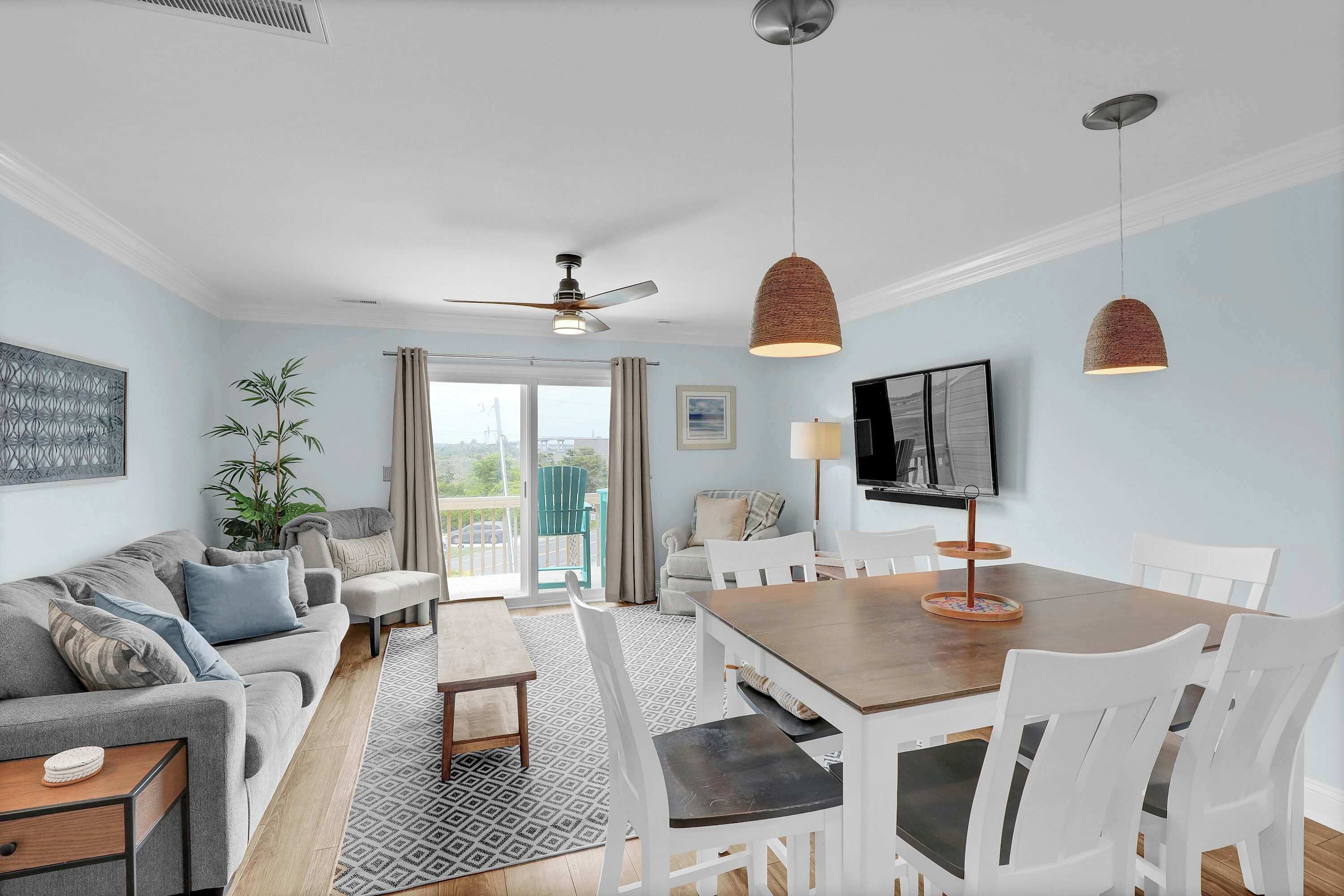 Un salon comprenant un canapé, une table à manger, des chaises, un ventilateur de plafond, des luminaires suspendus, un téléviseur et une vue sur l’extérieur, visible à travers une porte vitrée.