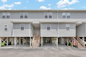 A multi-story residential building with a covered parking area, wooden stairs, and an American flag. - Lazy Day Lookout - New Listing (Surf City)