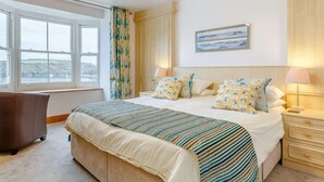Een slaapkamer met een groot bed, een bureau, een stoel, een raam met uitzicht en een kroonluchter.