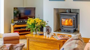 Een woonkamer met een televisie, een bijzettafeltje met een bloevas, een open haard en een bank.