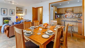 Een eethoek met een houten tafel voor vier personen, een bank en een keuken met houten kastjes.