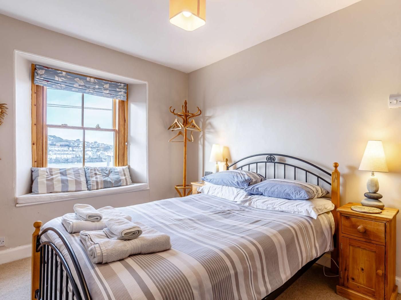 Une chambre à coucher avec un lit, une fenêtre donnant sur un beau paysage, un porte-manteau, des lampes de chevet et une table de chevet.
