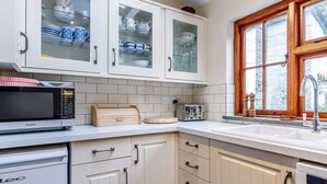 Una cocina con armarios blancos, microondas, tostadora y una ventana con marcos de madera.