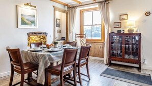 Comedor con mesa de madera, sillas, chimenea y un aparador con puertas de vidrio.