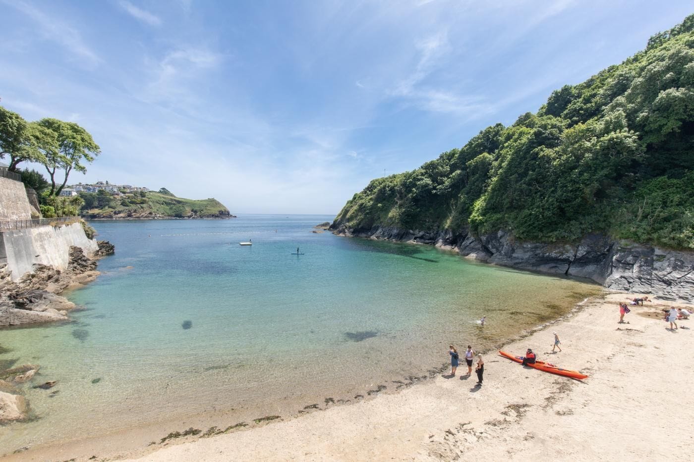 A coastal beach with clear water, rocky cliffs, and a sandy shore.
