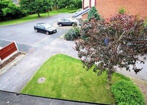 Ein Wohnweg mit zwei Autos, einem Rasen und einem Baum.