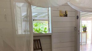 A room with a bed, a chair, a window with a view of greenery, and a door with a sign.