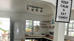 A kitchen with a white brick island, wooden stools, a refrigerator, and a sign that reads 'KEEP CALM & EAT CANDY'.