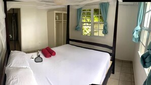 A single bed with white bedding and two red pillows, a window with curtains, a wardrobe, and a door leading to another room.