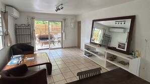 A living room with a dark wooden table, a sofa, a TV, and a sliding glass door leading to an outdoor area.
