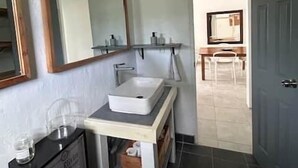 Un bany amb un lavabo blanc, un mirall, un armari negre i una porta que dona a una zona de dinar.