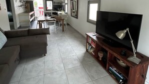 Àmplia zona d'estar amb un televisor gran, un moble de divinització de fusta i una zona de dinar.