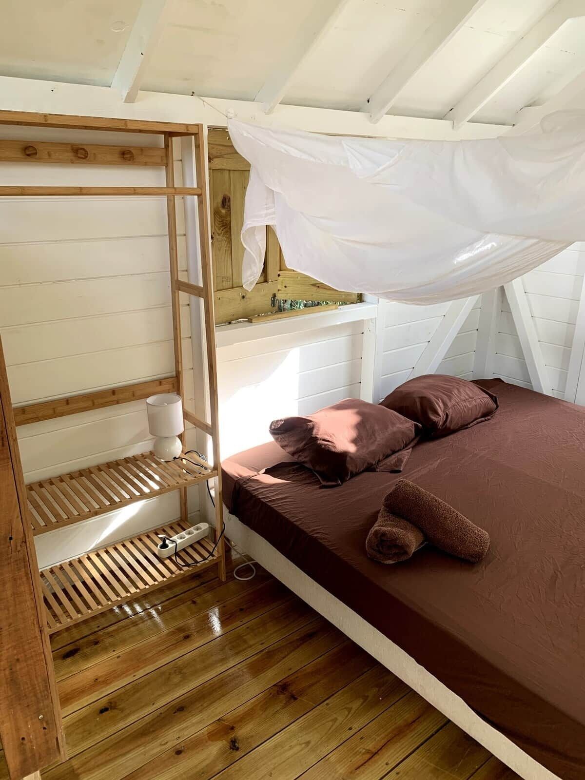 A single bed with a canopy, wooden shelves, and a bedside table in a room with sloped ceilings.