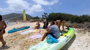 A beach with kayaks, a windsurf board, and people.