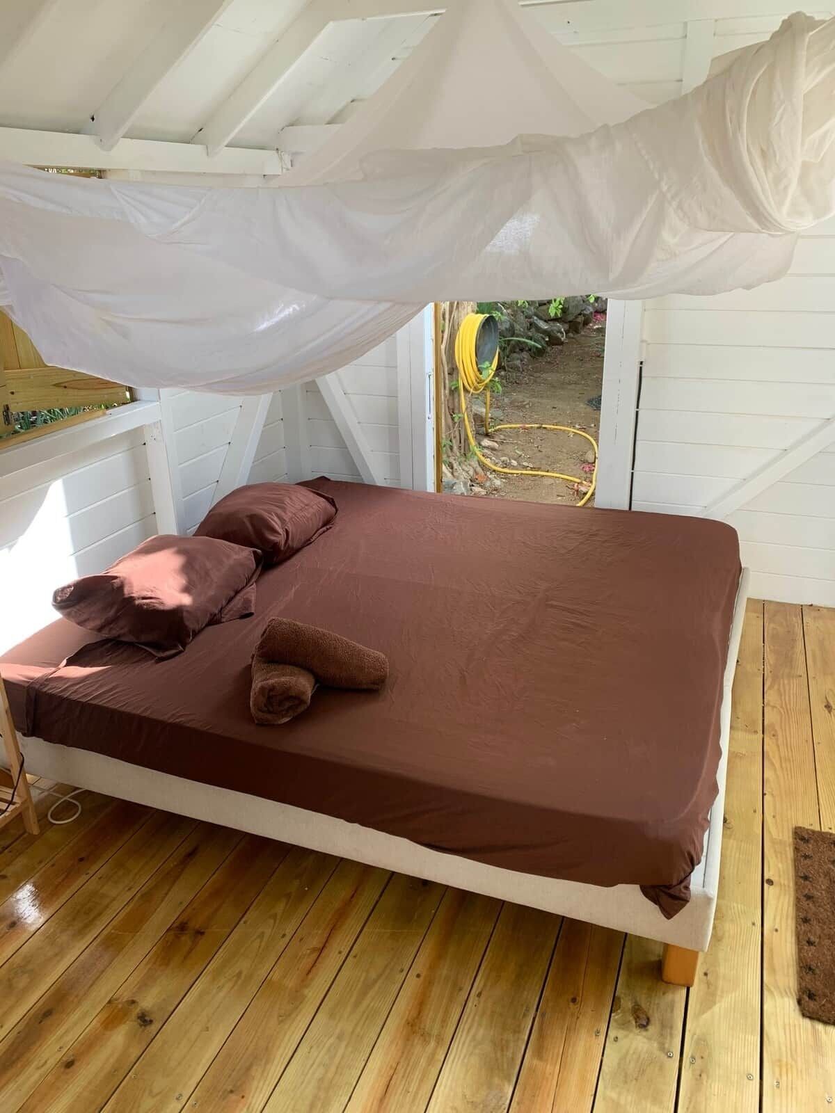 Una cama individual con colchón y almohadas marrones, un dosel blanco y suelo de madera.
