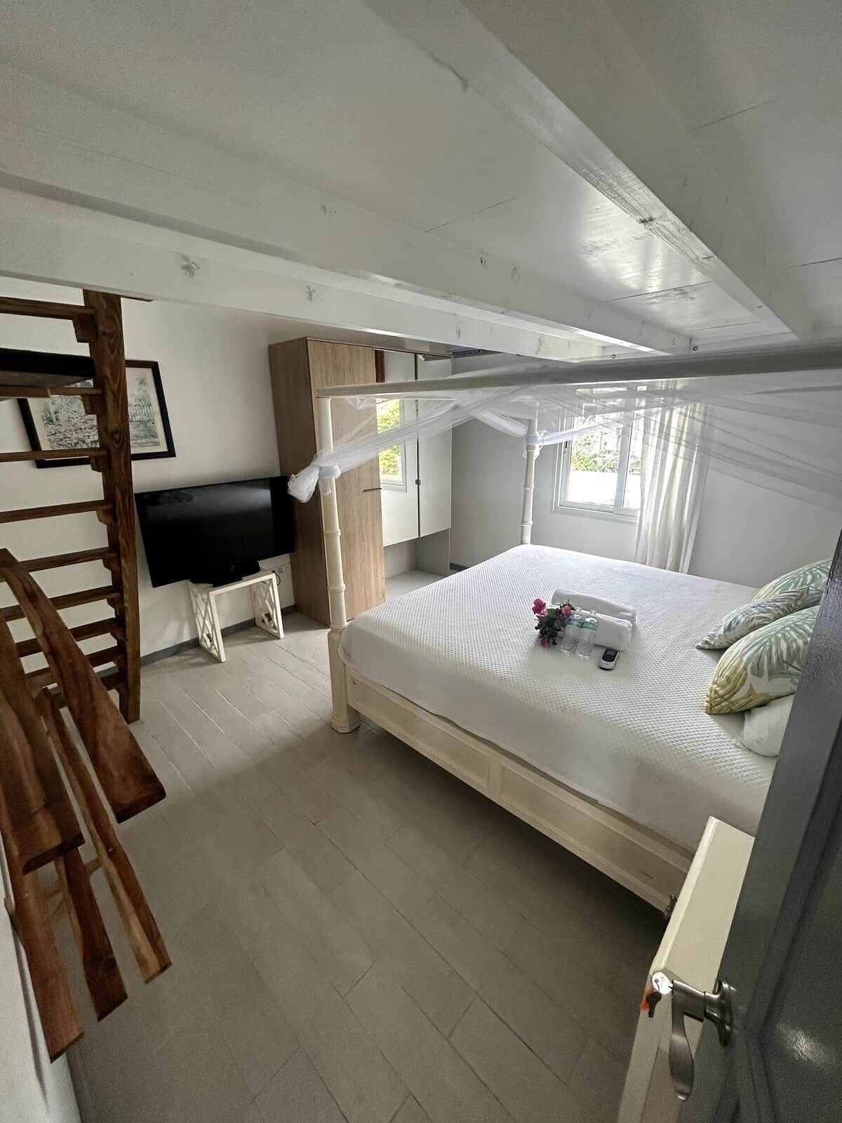 Ein Schlafzimmer mit Himmelbett, einer Holzleiter, einem Fernseher, einem Schreibtisch und einem Kleiderschrank.