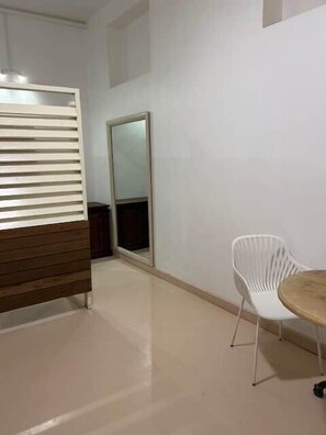 Ein Zimmer mit einer hölzernen Bank, einem weißen Stuhl, einem runden Tisch und einem großen Spiegel an der Wand.