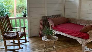 Een houten terras met een schommelstoel, een comfortabele bank en een kleine tafel met een plant.