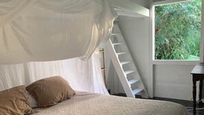Ein Schlafzimmer mit einem großen Bett, einer Leiter und einem Fenster mit Blick auf Grünflächen.