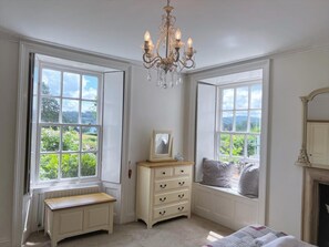 A room with large windows, a wooden bench, a dresser with drawers, a chandelier, and a fireplace. - 3 Bed in Ambleside (oc-62587) (Claife)