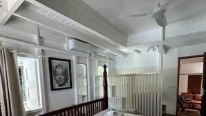 Un dormitori amb un llit gran, un ventilador de sostre, un radiador i una finestra amb cortines.