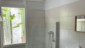 Bany amb vàter, rentapel, dutxa i finestra amb vista a vegetació.