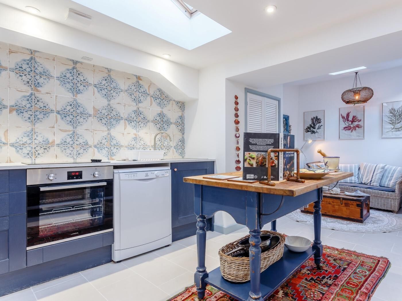 Een moderne keuken met een vaatwasser, oven en een blauwe tafel met een mand.