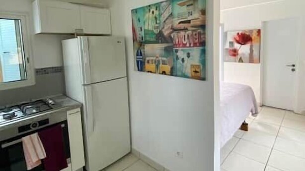 Een kleine keuken met een koelkast, fornuis en magnetron. Er hangt een schilderij aan de muur en er is een plafondventilator.